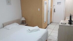 Una habitación de hotel con cama, escritorio, computadora, lámpara y puerta.