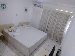 Quarto de hotel com uma cama de solteiro, mesa de cabeceira, ar condicionado fixado na parede e janela com cortinas.