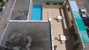 Un área de piscina en la azotea con piscina azul, asientos al aire libre y una sección cubierta.