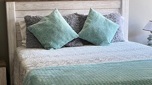 A bed with a textured white bedspread and two teal pillows.