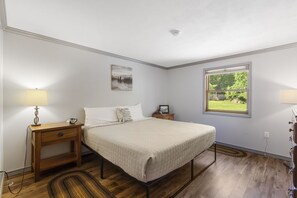 Ein Schlafzimmer mit Bett, Nachttischen, einer Lampe, einem Fenster mit Aussicht und einem Bild an der Wand.