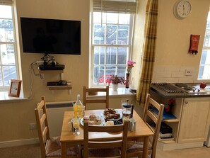 Un comedor con una mesa preparada para el desayuno, un televisor montado en la pared y una ventana con persianas.