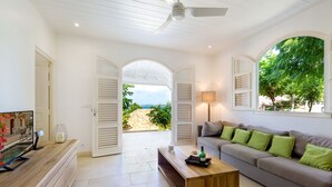 A spacious living area with a wooden coffee table, a sofa with green cushions, and a television on a wooden cabinet. - Maison Cerisier accès mer (Le François)
