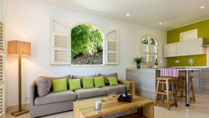 A modern living room with a sofa, coffee table, and a view of a garden through a window with shutters. - Maison Cerisier accès mer (Le François)