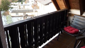 A balcony with a wooden railing, a bench with a red cushion, and a view of houses in the background. - Hotel Ockenheim (Ockenheim)