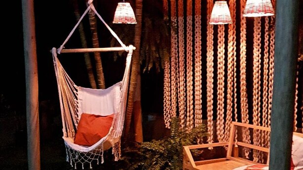 Un sillón hamaca y un banco de madera bajo una pérgola de madera con lámparas colgantes.