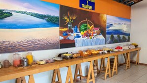 Una mesa de buffet con diversos alimentos y bebidas, con un fondo de dos grandes cuadros de paisajes.