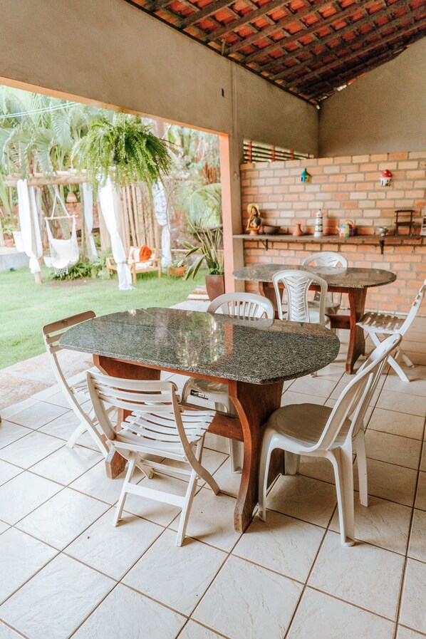 An outdoor patio with a brick wall, a round table, and white plastic chairs.