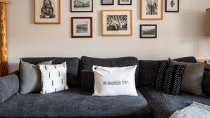 A modern living room with a grey sofa, multiple framed artworks on the wall, and a white pillow with text. - Outpost: Pitchfork 434 - 1 bedroom near Snow King! (Jackson)
