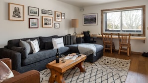 A living room with a dark grey sofa, a wooden coffee table, and a large window with a view of trees. - Outpost: Pitchfork 434 - 1 bedroom near Snow King! (Jackson)