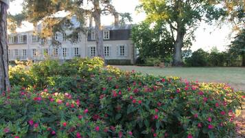 Un grand bâtiment à la façade symétrique, entouré d’un jardin bien entretenu où poussent des arbustes à fleurs.