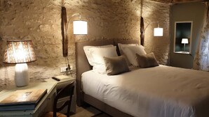 A bedroom with a stone wall, a bed with white bedding, two bedside lamps, a desk with a lamp, and a chair. - Colivault (Cande-sur-Beuvron)