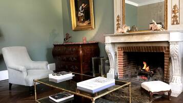 Una sala de estar con chimenea, un sillón blanco, un aparador de madera y una mesa de centro de vidrio con libros.