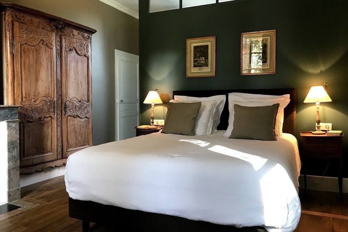 A neatly made bed with white linens, two bedside lamps, and a dark wooden wardrobe.