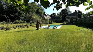 A grassy backyard with a swimming pool, a stone wall, and a house in the background. - Colivault (Cande-sur-Beuvron)