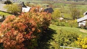 Ländliche Landschaft mit einem Haus, umgeben von Grün, und einem Tal im Hintergrund.