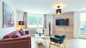 A modern living room with a red sofa, a white coffee table, a blue armchair, and a TV mounted on a wooden wall. - Apartment Winterberg - Stylish (Winterberg)