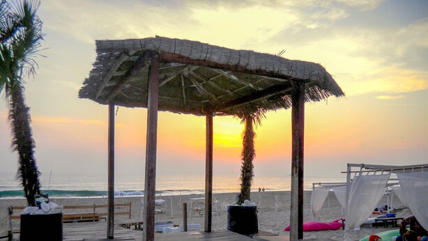 A beach with a wooden deck, a thatched-roof pavilion, and beach chairs. - Destiny - Caparica apartment (Costa da Caparica)