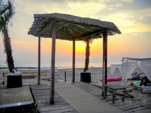 A beach with a wooden deck, a thatched-roof pavilion, and beach chairs. - Destiny - Caparica apartment (Costa da Caparica)