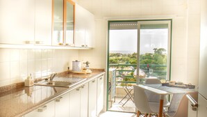 A kitchen with a view of the city, a dining area with chairs and a table, and a balcony with a view. - Destiny - Caparica apartment (Costa da Caparica)