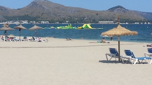 Una playa con tumbonas, sombrillas y una vista despejada del mar y las montañas al fondo.