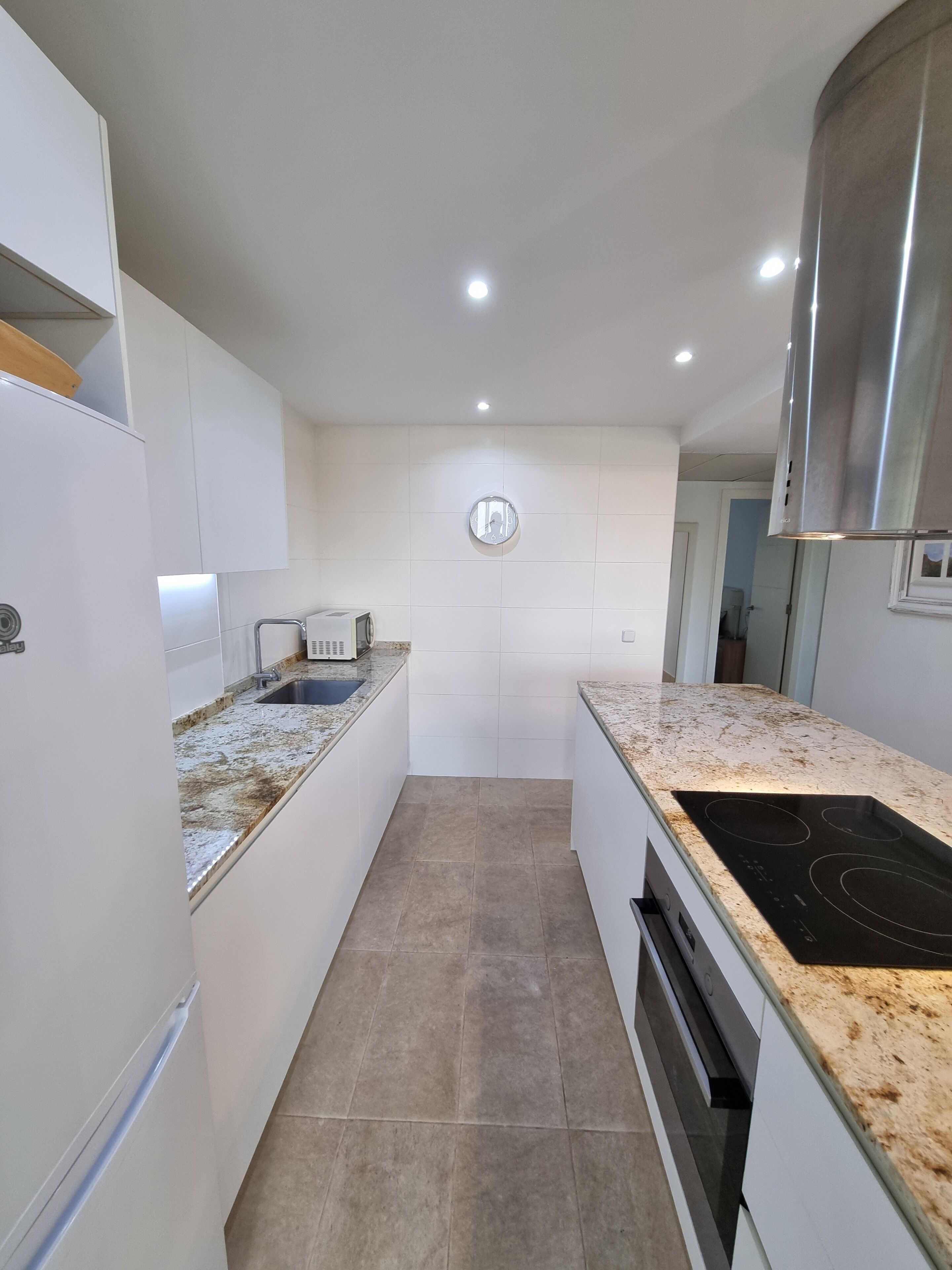 Una cocina moderna con armarios blancos, una campana extractora de acero inoxidable, horno empotrado y encimera de granito.