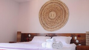 A neatly made bed with white linens and rolled towels, a wooden headboard, and a woven wall hanging above it. - Pousada Francês Praia (Marechal Deodoro)