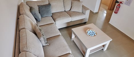 Ett modernt vardagsrum med en beige hörnsoffa, ett vitt soffbord och en matplats i bakgrunden.