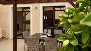 An outdoor patio with wicker furniture, a table with a bottle and glass, and a pergola structure. - Kyklades Angie Resort (Paralimni)