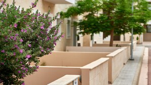 A row of beige apartment buildings with balconies, a tree with purple flowers, and a lamppost. - Kyklades Angie Resort (Paralimni)