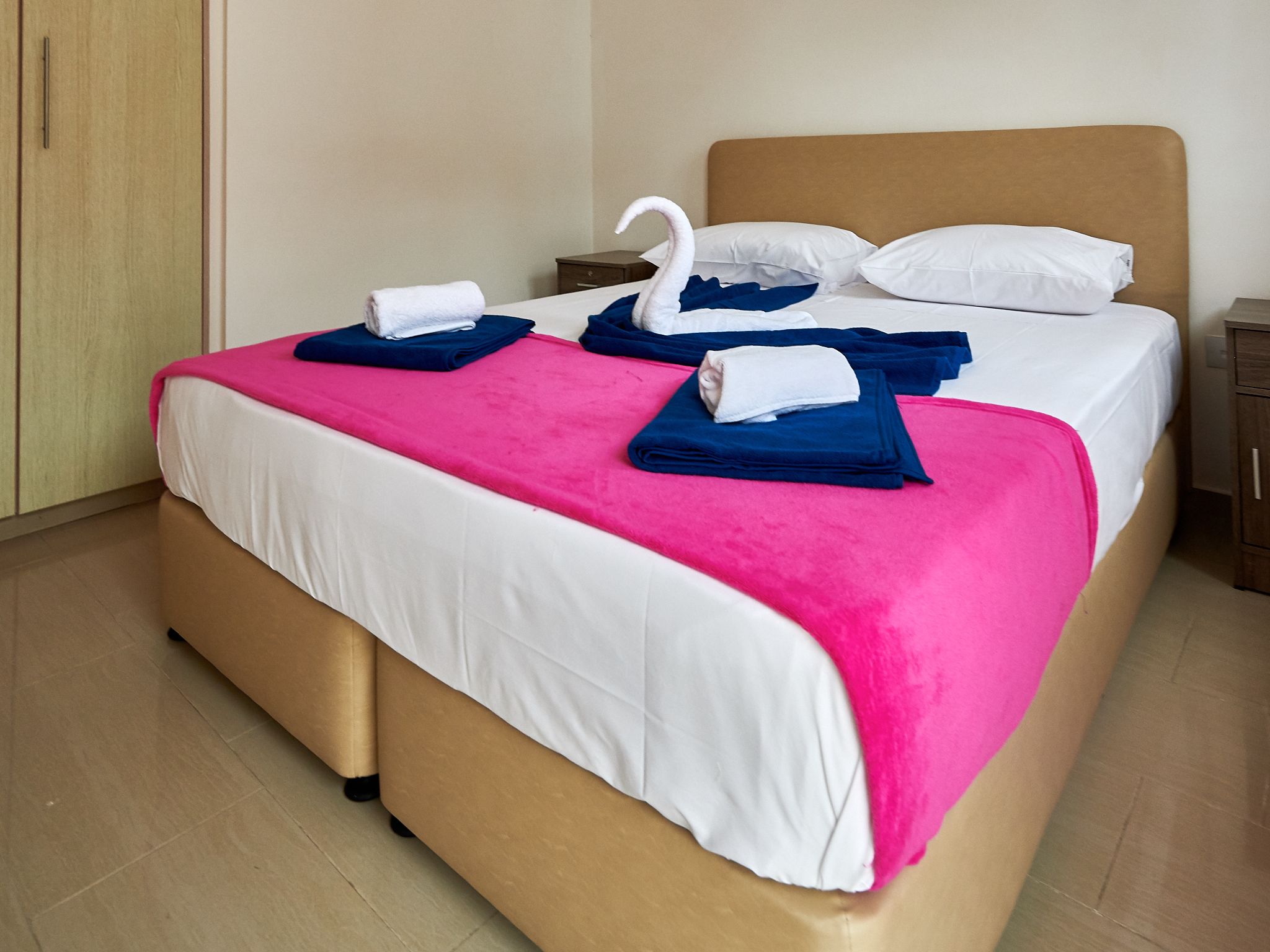 A hotel room with a bed, pillows, and a swan-shaped towel.