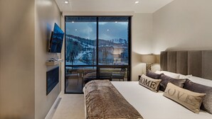 Une chambre avec un grand lit, un téléviseur fixé au mur et une vue sur un paysage enneigé, visible à travers une grande fenêtre.