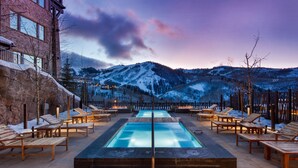 Un espace piscine avec des chaises longues en bois et une vue sur des montagnes enneigées.