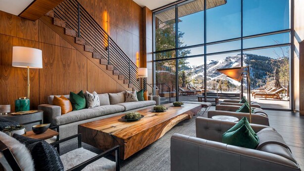 Un salon moderne avec un grand canapé, une table basse en bois et une vue sur un paysage montagneux grâce à de grandes fenêtres.