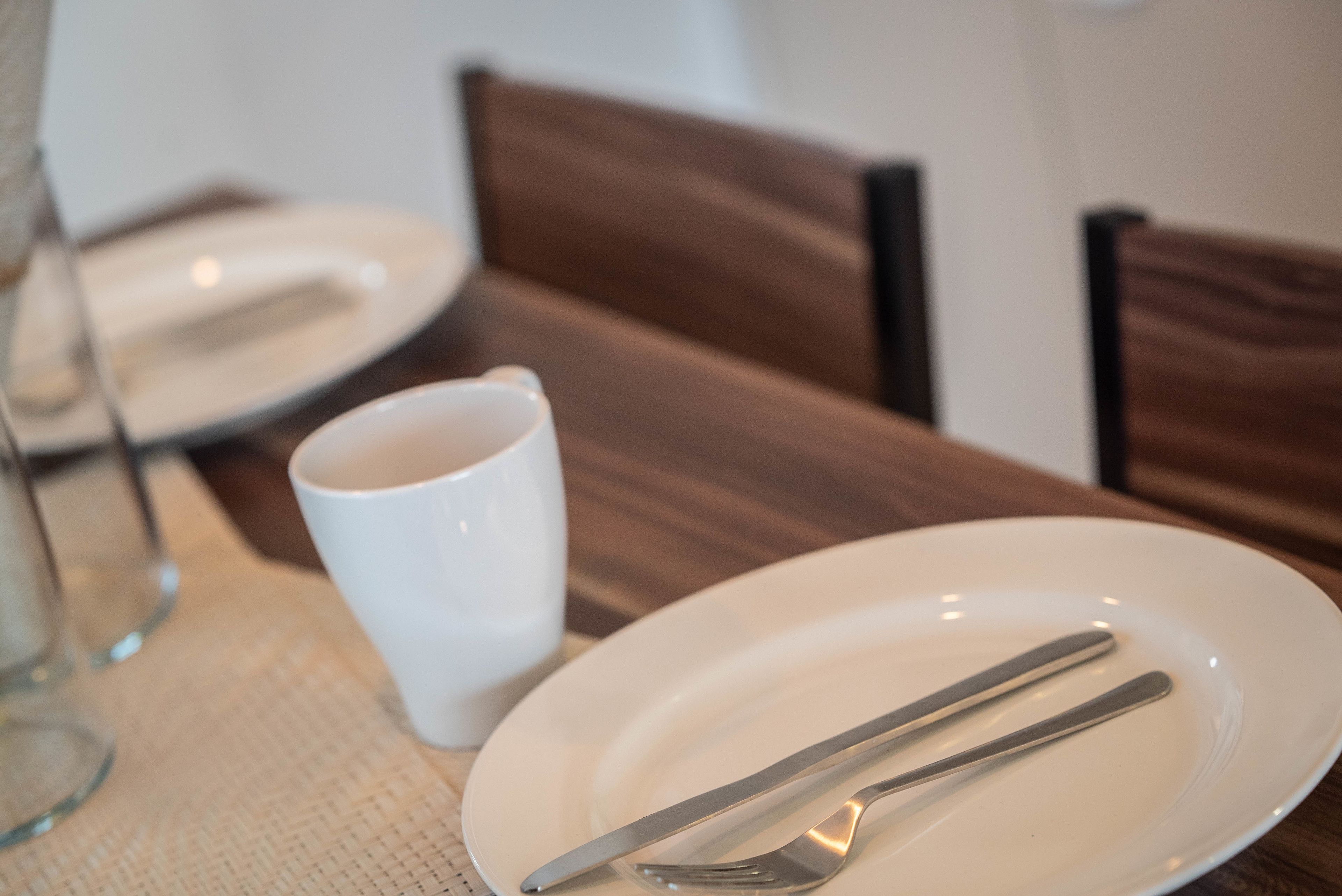 A dining table with a white plate, a white mug, and a fork and knife set.