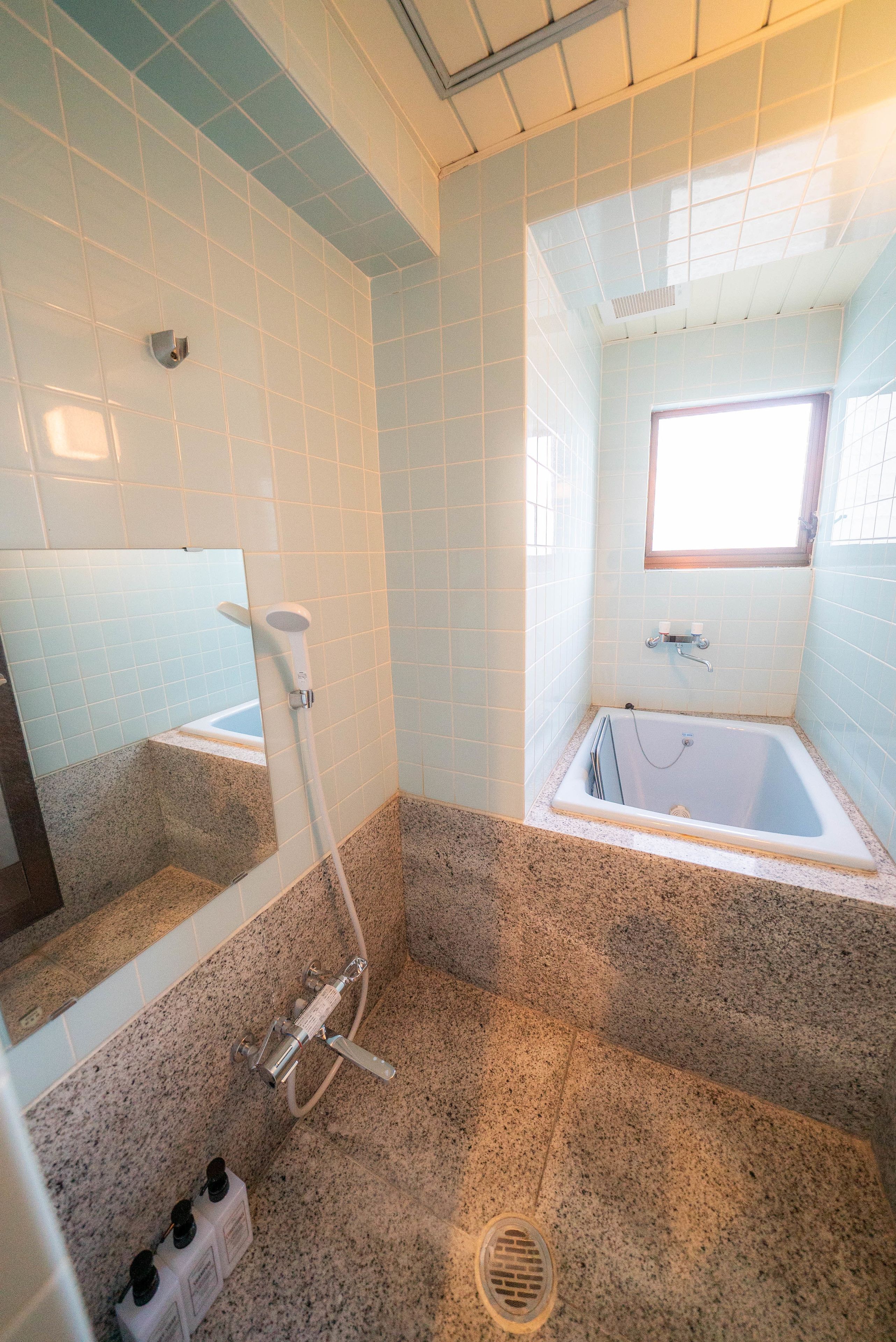 A bathroom with a shower, a bathtub, a window, and a mirror.