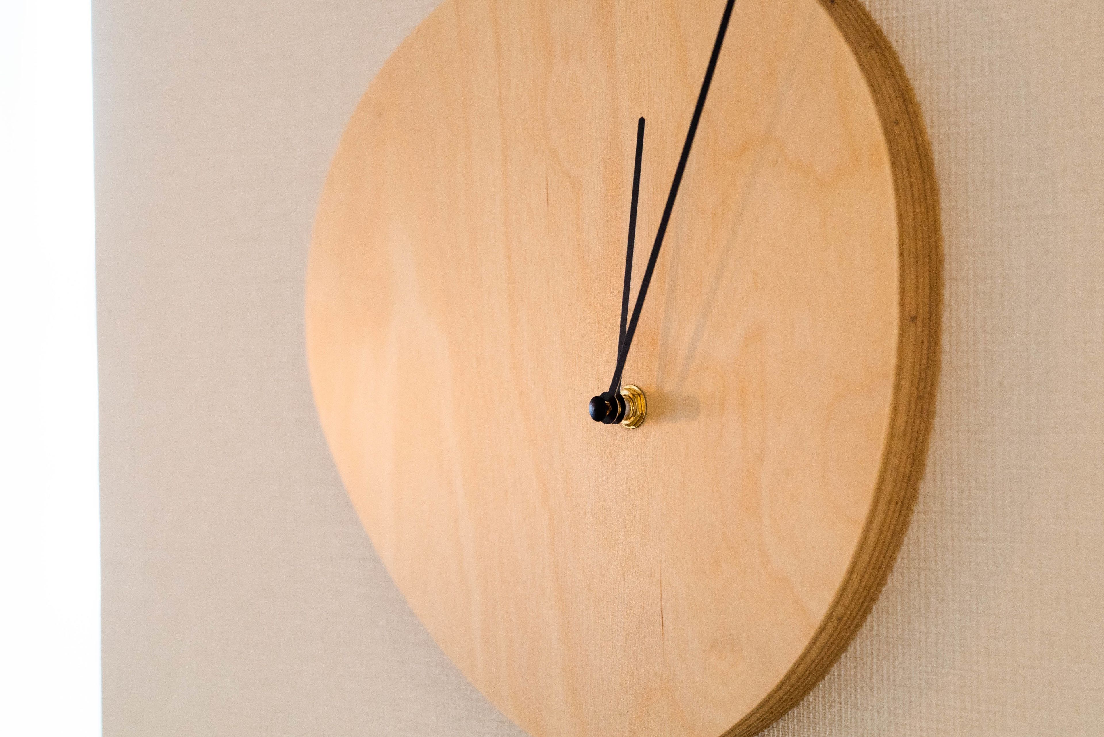 En rund väggklocka i trä med en minimalistisk design, med en svart och guldglänsande pendel.