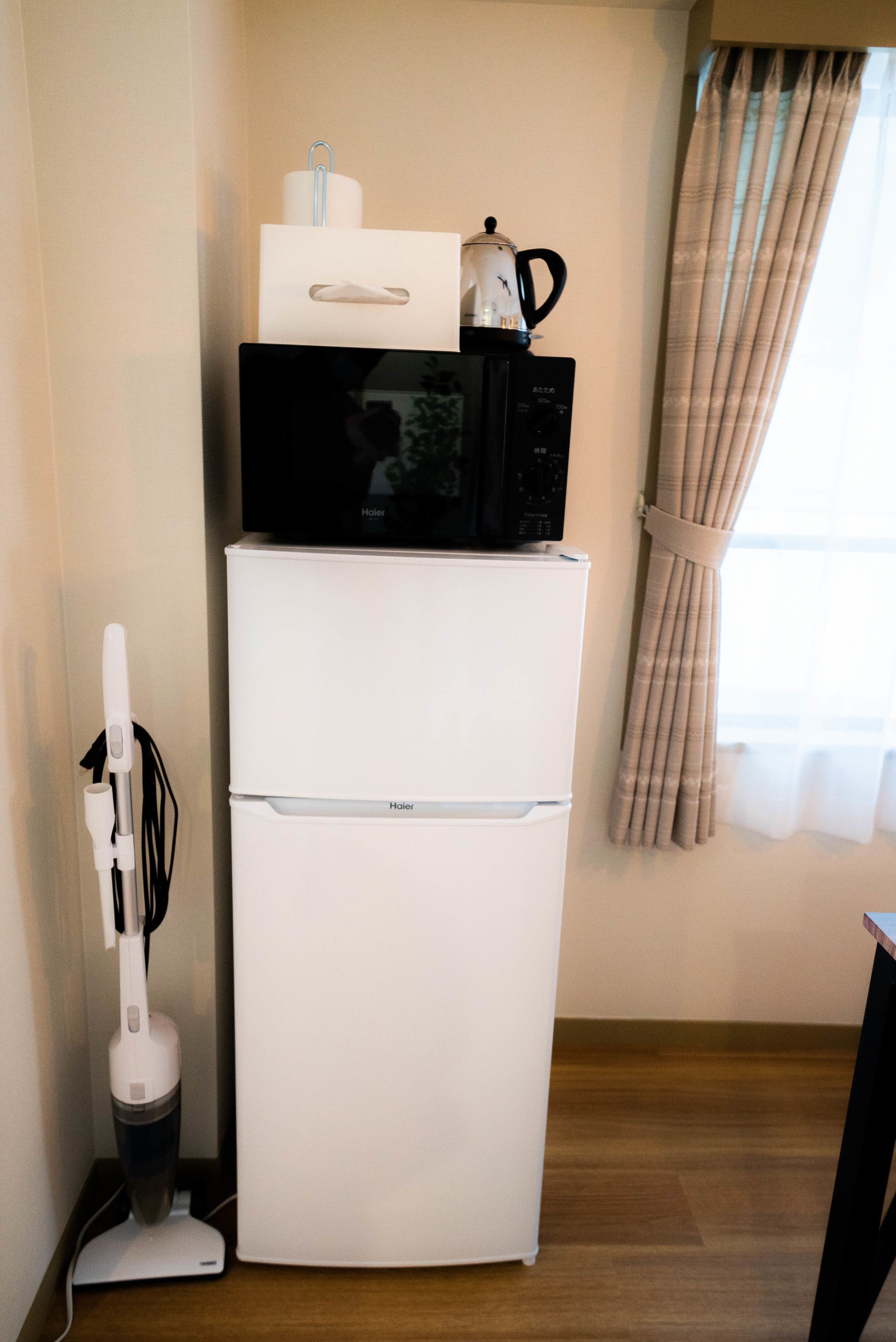 A compact kitchenette with a white refrigerator, a microwave, and a coffee maker on top.