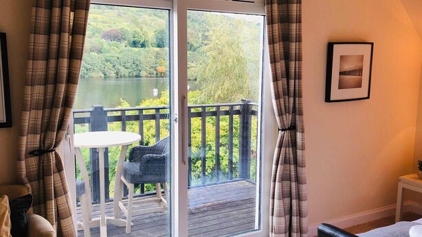 A room with a sliding glass door leading to a balcony with a table and chairs, overlooking a lake and greenery. - Chefs cottage. Idyllic 18th century cottage. (Kenmore)
