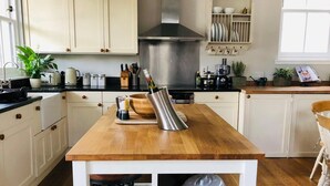 A kitchen with white cabinets, a wooden island, a stainless steel range hood, and a built-in shelf with dishes and a coffee machine. - Chefs cottage. Idyllic 18th century cottage. (Kenmore)