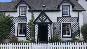 A traditional white building with black window frames and a white picket fence in front. - Chefs cottage. Idyllic 18th century cottage. (Kenmore)