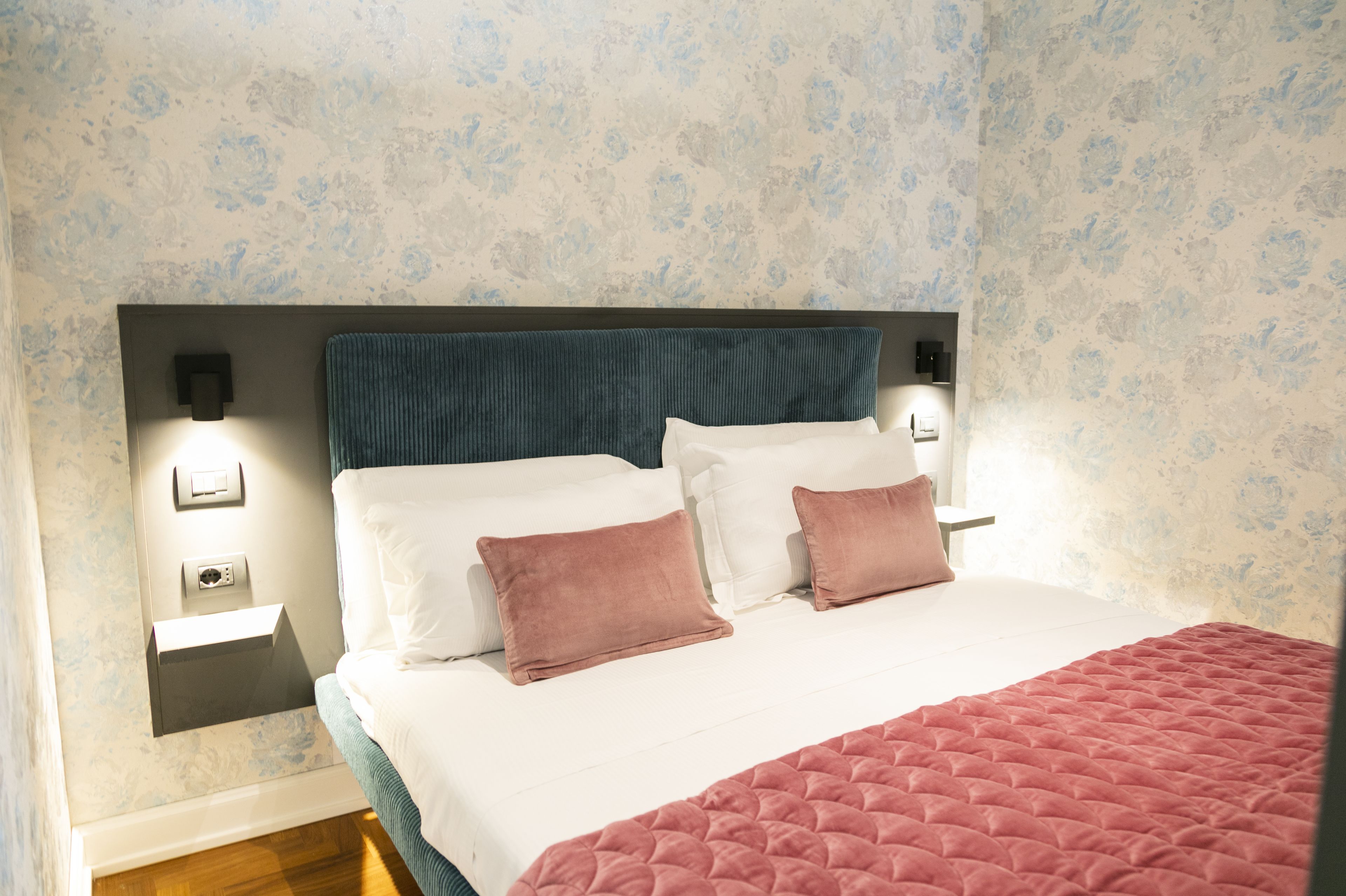 Una cama bien hecha con almohadas blancas y rosadas, un cabecero verde aguamarina y una colcha rosa.