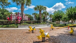 A playground with yellow spring-mounted toys and a red building in the background. - EV_76604 - 3 Bed 2 Bath Condo with Access to Resort Amenities (Kissimmee)