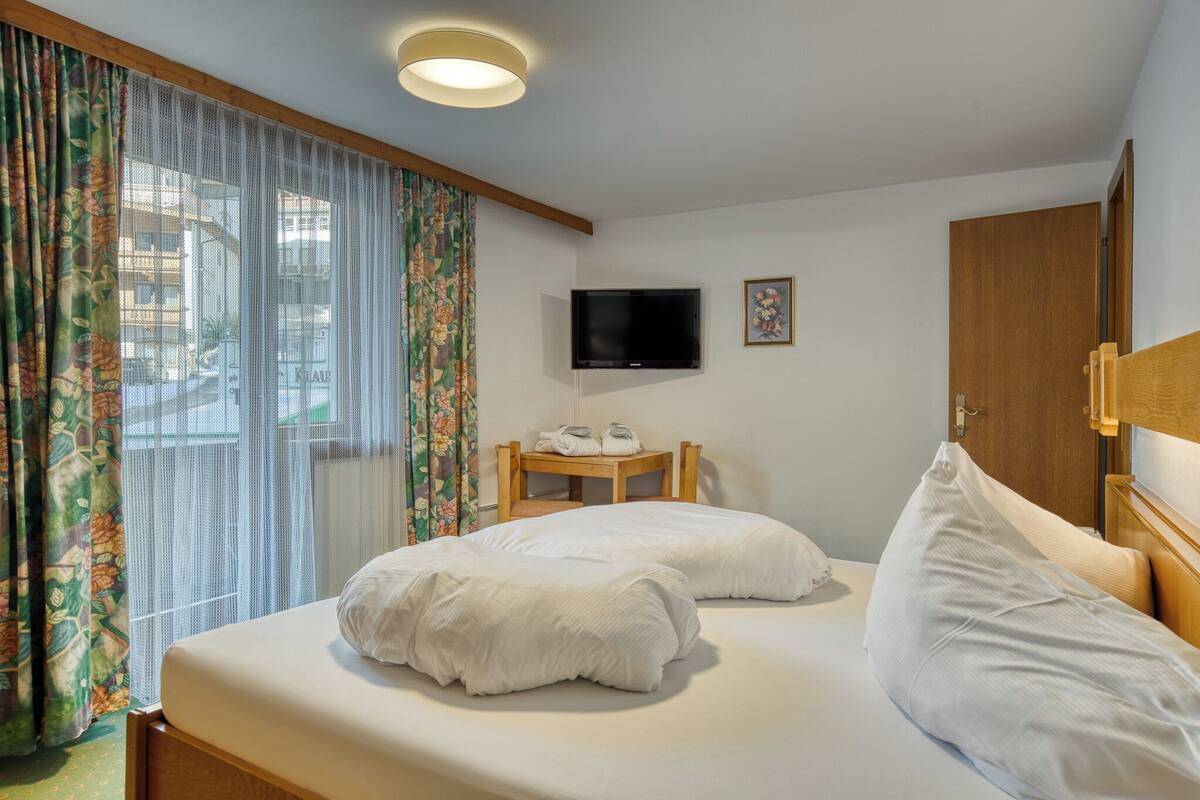 A hotel room with a bed, a desk with a chair, a television, and a door.