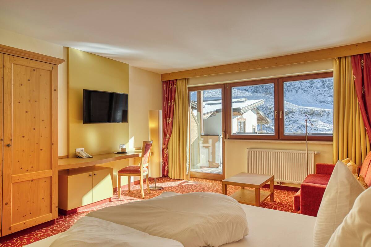 A hotel room with a bed, a desk, a chair, a TV, and a view of mountains through large windows.
