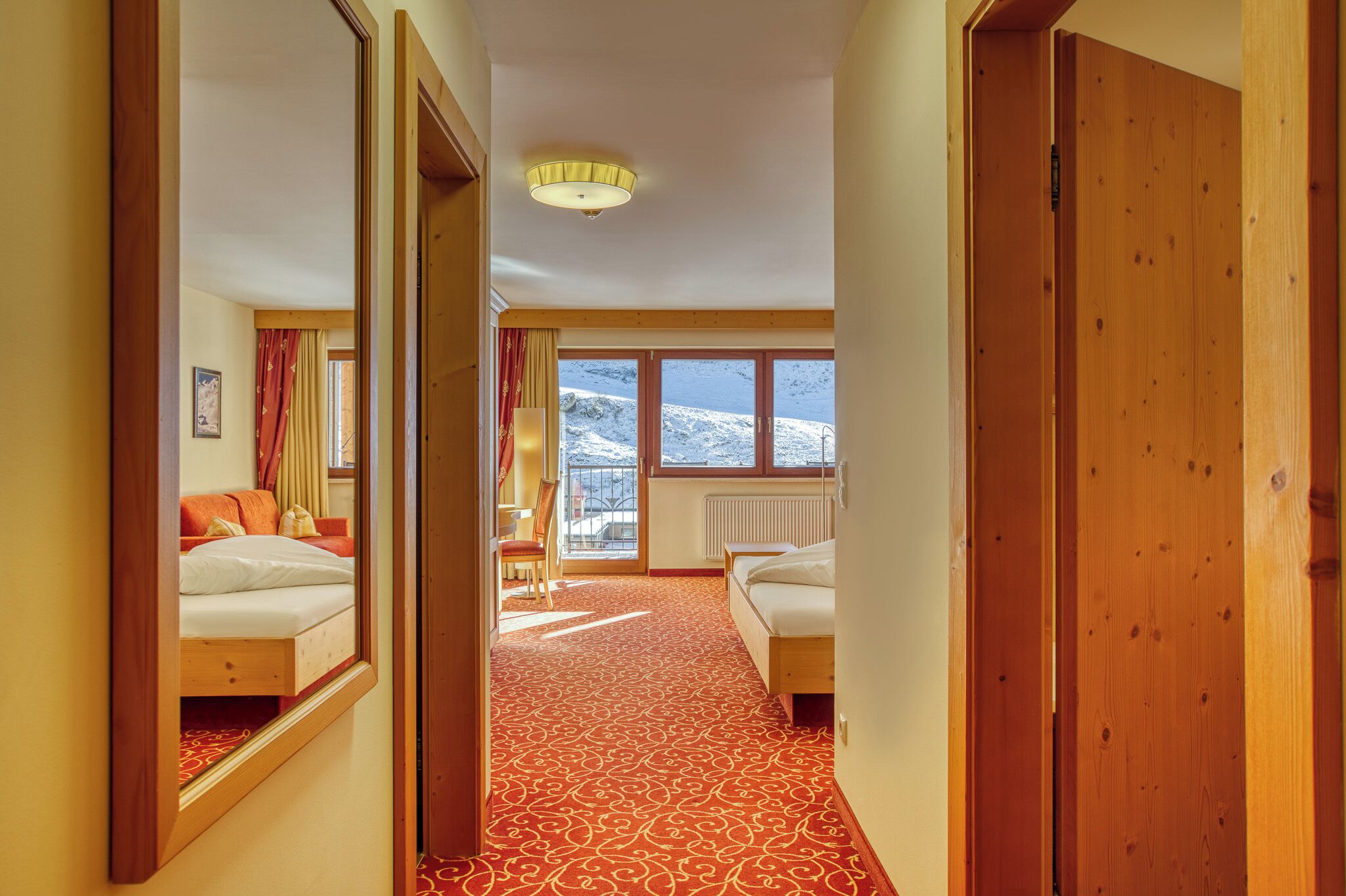 A hotel room with a wooden floor, two beds, a large window with a view of snow-covered mountains, and a ceiling light.