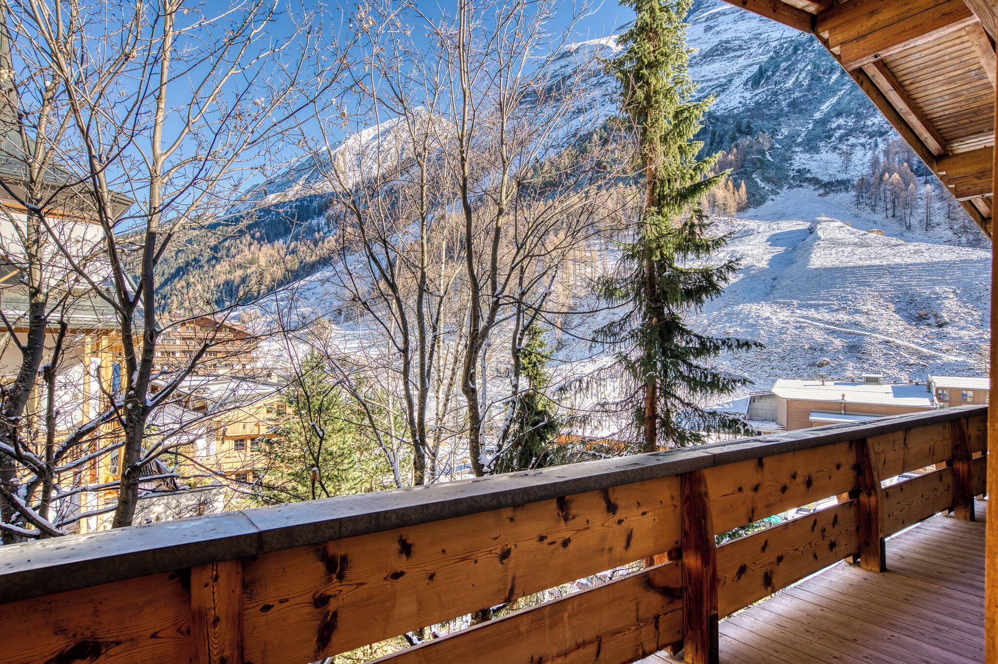 A wooden balcony with a view of snow-covered mountains and trees.