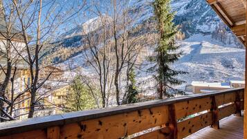 A wooden balcony with a view of snow-covered mountains and trees.