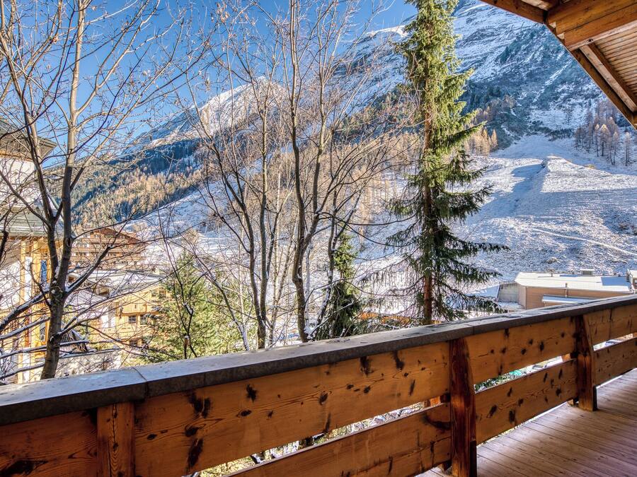 A wooden balcony with a view of snow-covered mountains and trees.