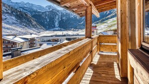 A wooden balcony with a view of snow-covered mountains and buildings below. - Hotel Klausnerhof (Tux)